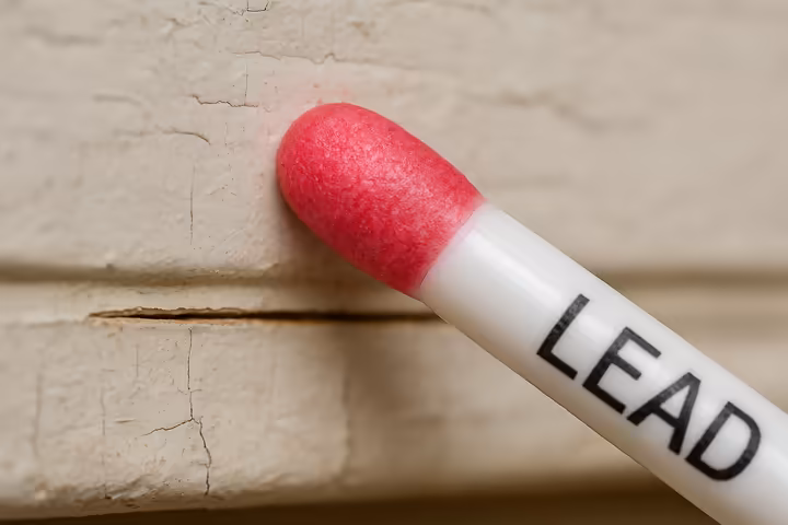 A close-up of an EPA-recognized lead test kit swab showing a bright red color, indicating a positive test for lead on a painted surface.